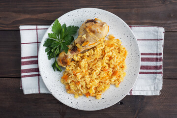 Delicious Asian pilaf, stewed rice with vegetables and chicken drumstick on a plate. Wooden rustic background. Copy space top view