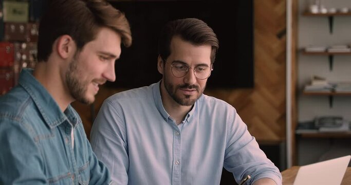 Concentrated skilled young 35s employee in eyeglasses discussing working issues with motivated male colleague in office, brainstorming project ideas. Smart supervisor coaching new intern at workplace.