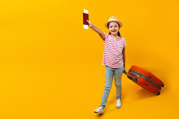 Travel concept. Happy child walks with suitcase and vaccination passport. Little girl on a yellow...