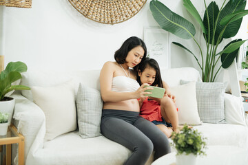 Happy family pregnant mother and little daughter taking selfie together, home interior