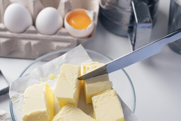 Girl preparing cookies in the kitchen, cutting butter, close-up. A woman prepares dough for delicious pastries. Step-by-step instructions. Mixing different ingredients for the dough. Background