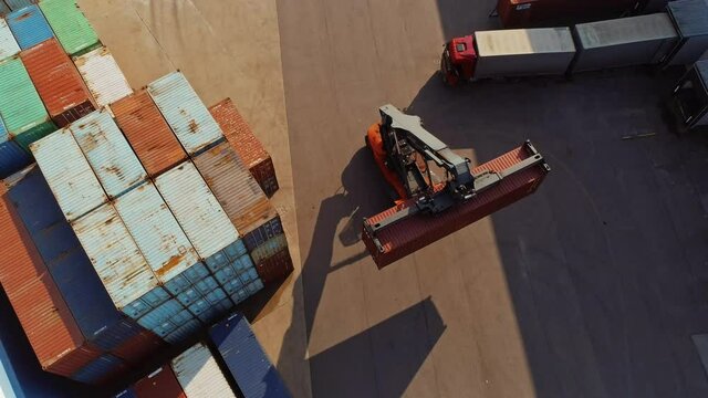 Aerial Drone Footage of a Container Handler Carrying a Large Red Cargo Container in a Shipyard Terminal
