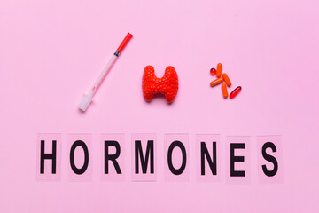 Word HORMONES, thyroid gland, pills and syringe on color background