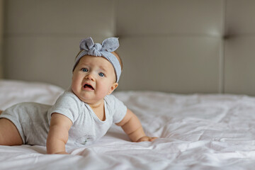 Caucasian blonde baby six months old lying on bed at home. Kid wearing cute gray clothing and headband. Bedroom decorated with flags.