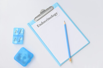 Clipboard with word ENDOCRINOLOGY and pills on white background