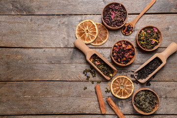 Bowls and spoons with dry tea leaves on wooden background