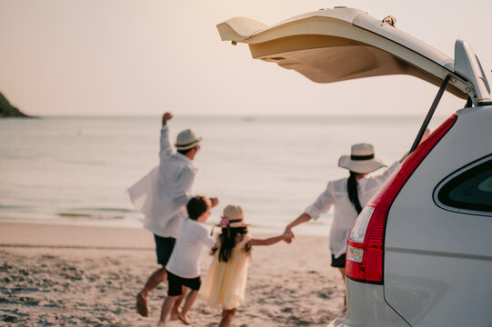 Asian Family Vacation Holiday, Happy Family Running On The Beach In The Sunset.Happy Family Is Running Into The Sea.Back View Of A Happy Family On A Tropical Beach And A Car On The Side.