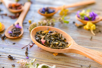 Spoons with dry tea leaves and flowers on wooden table