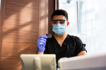 Stock photo of a dentist wearing medical gloves and glasses, looking at the x-ray image, front view of the x-ray of tooth