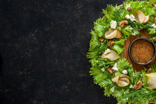 Light Diet Salad With Pear, Nuts And Blue Cheese. The Salad Is Laid In The Form Of A Wreath On A Round Wooden Board With Sauce In The Center On A Dark Background. Copy Space Top View