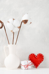 A vase with cotton, red heart and a gift against the background of a light wall, a concept, a postcard for Valentine's Day. Copy space.