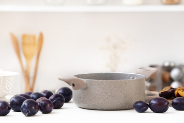 Pot and fresh plums on table in kitchen