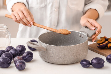 Woman adding sugar into pot on table