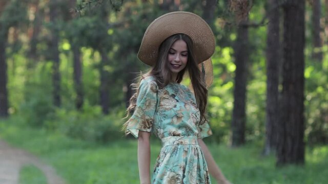 A young attractive girl in a hat running in a summer Park at sunset, in the woods. Beautiful woman enjoying the nature outdoors.Slow motion