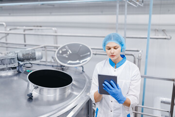 Food automated modern industrial production. Operator worker woman checks steel tanks with tablet...