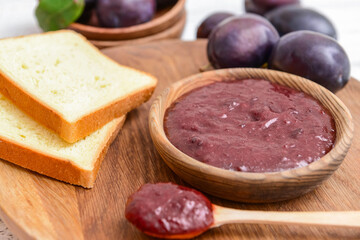 Bowl with delicious homemade plum jam on wooden board
