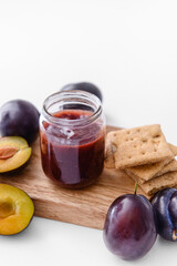 Glass jar with delicious homemade plum jam on white background