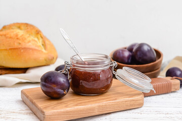 Glass jar with delicious homemade plum jam on wooden background