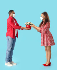 African-American couple in medical masks and with flowers on color background. Valentine's Day celebration