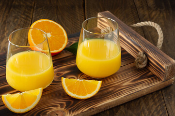 Fresh orange juice in glasses with cut oranges on wooden tray. Rustic still life with citrus fruits
