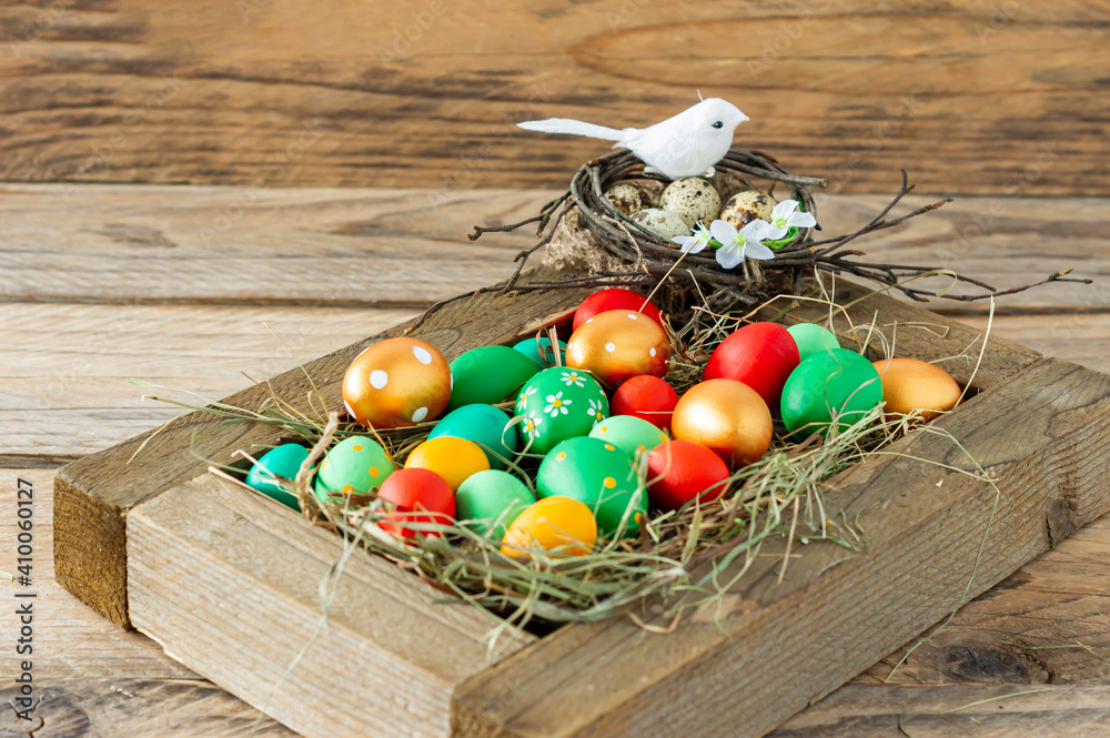 Wall mural Colorful hand painted easter eggs and nest with bird in wooden box on wooden table.