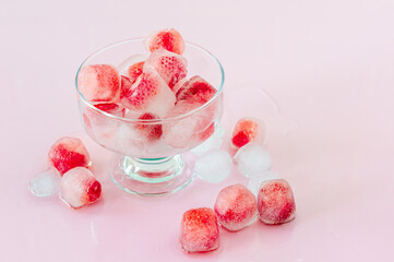 Ice cubes with strawberries on pink background.