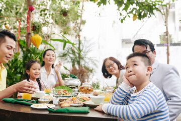 Family looking at adorable pensive little boy sitting at dinner table
