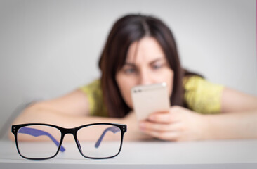 In the foreground there are glasses for vision, in the background a girl squints into a smartphone....