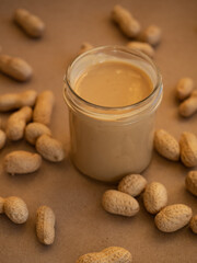 Homemade peanut butter in a glass jar with peanuts in shells scattered around on a craft background in natural light