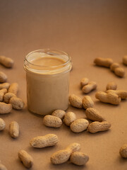 Homemade peanut butter in a glass jar with peanuts in shells scattered around on a craft background in natural light