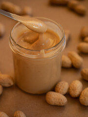 Homemade peanut butter in a glass jar with peanuts in shells scattered around on a craft background in natural light