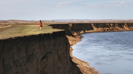 lone girl in red dress gazing on the water from the cliff