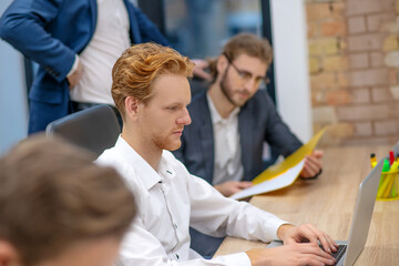 Obraz premium Redhaired man working at laptop and colleague managers