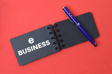 Top view of pen and notebook written with text E-BUSINESS over red background. 