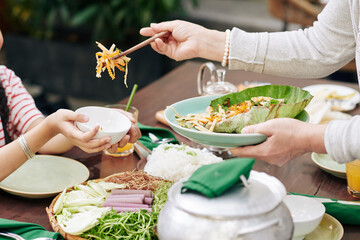 Cropped image of grandmother putting salad in plate of granddaughter at family dinner