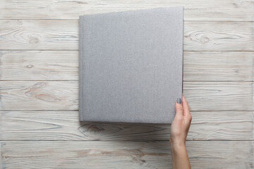 closed grey wedding photo album isolated on wooden background.
person opens a photobook.
womans fingers touch a family photoalbum. womans hand holding family photo book with space for text