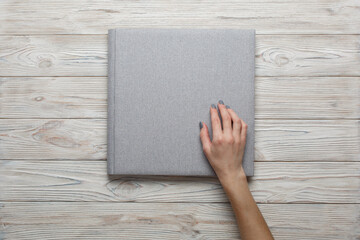 person touch and open a photobook.
Family photoalbum on the table.
womans hand holding a grey family photo album with copy space for text. stylish wedding photo album on light background
