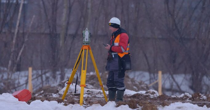 Excavation at a construction site in winter, a surveyor with a theodolite doing his job, surveying the area for the construction of buildings and structures, for laying roads 