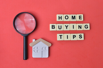 Top view of toy house, magnifying glass and scrabble letters with text HOME BUYING TIPS over red...