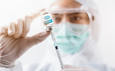 Scientist in PPE(personal protective equipment) and wear face mask protective gloves holding coronavirus vaccine in glass bottle on white background.