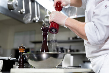 Professional chef in white uniform salts king prawns. Wooden salt grinder