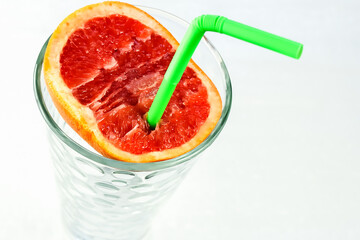 Half a juicy grapefruit with a green drinking straw in a glass. A healthy and tasty citrus drink highest in vitamins.