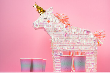 Party unicorn pinata and disposable cups on pink background