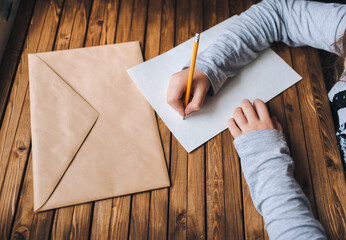 Children's hands write a letter. A brown envelope, a white sheet of paper and a pencil. Distance...