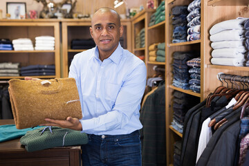 Confident salesman demonstrating warm sweaters in menswear boutique
