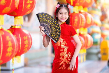 little Asian girl wearing red traditional Chinese cheongsam and holding a Fanningand lanterns with...