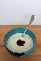 A healthy bowl with yoghurt, jam and oats under yoghurt for breakfast with spoon on wooden table