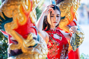 Portrait beautiful smiles Asian young woman wearing red traditional Chinese cheongsam decoration and holding a Chinese Fanning for Chinese New Year Festival at Chinese shrine in Thailand