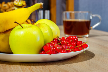 Dish with fresh green apples and red currant berries and blurred glass cup of tea at background
