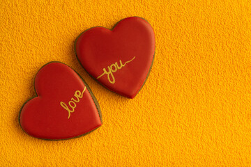 Obraz premium Two heart-shaped cookies with red sugar icing and inscription LOVE YOU, yellow background. Copy space